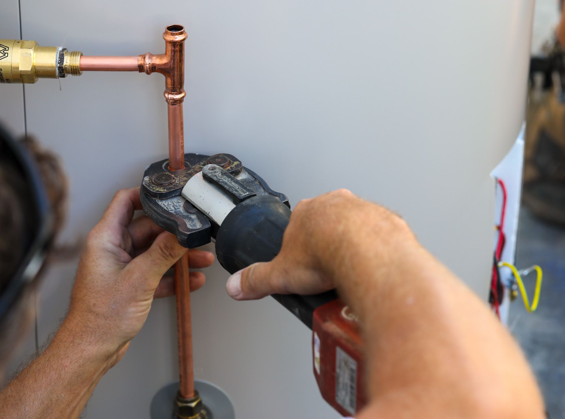 A man is working on a copper pipe with a drill.