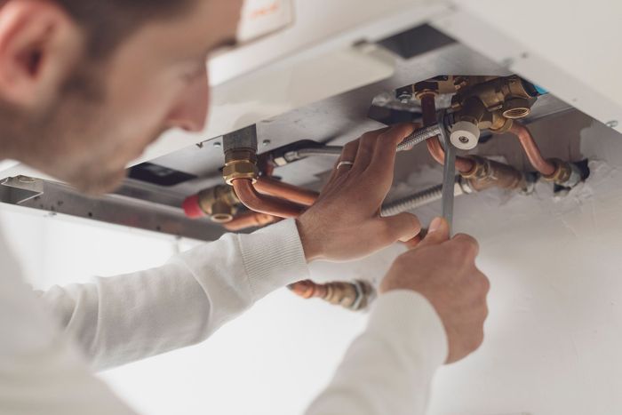 A man is fixing a water heater with a wrench.