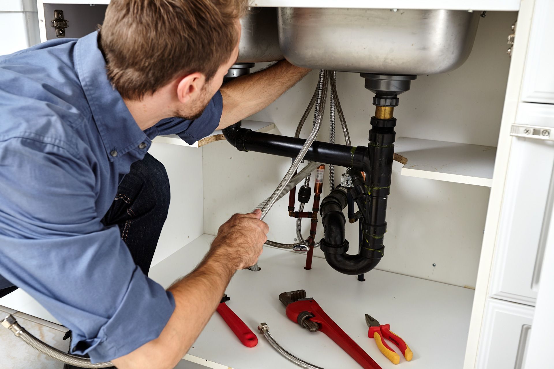 A plumber is fixing a sink in a kitchen.