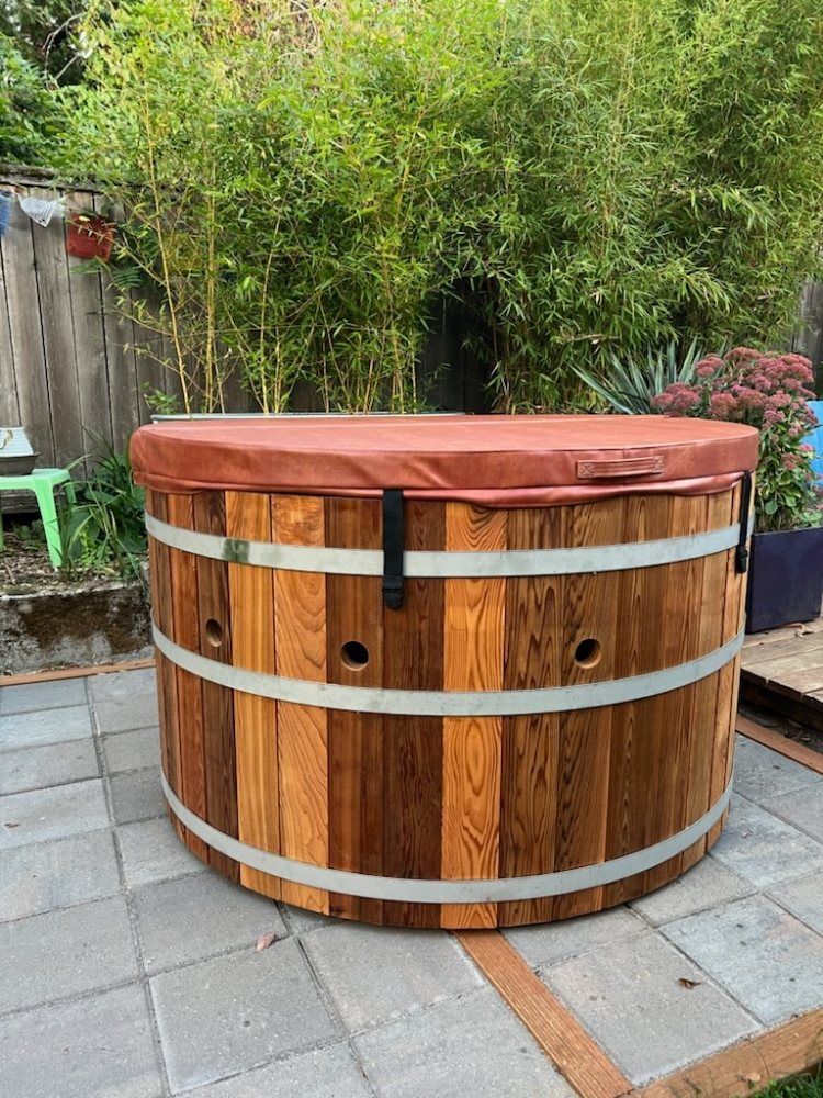 A wooden hot tub with a red cover is sitting on a patio.