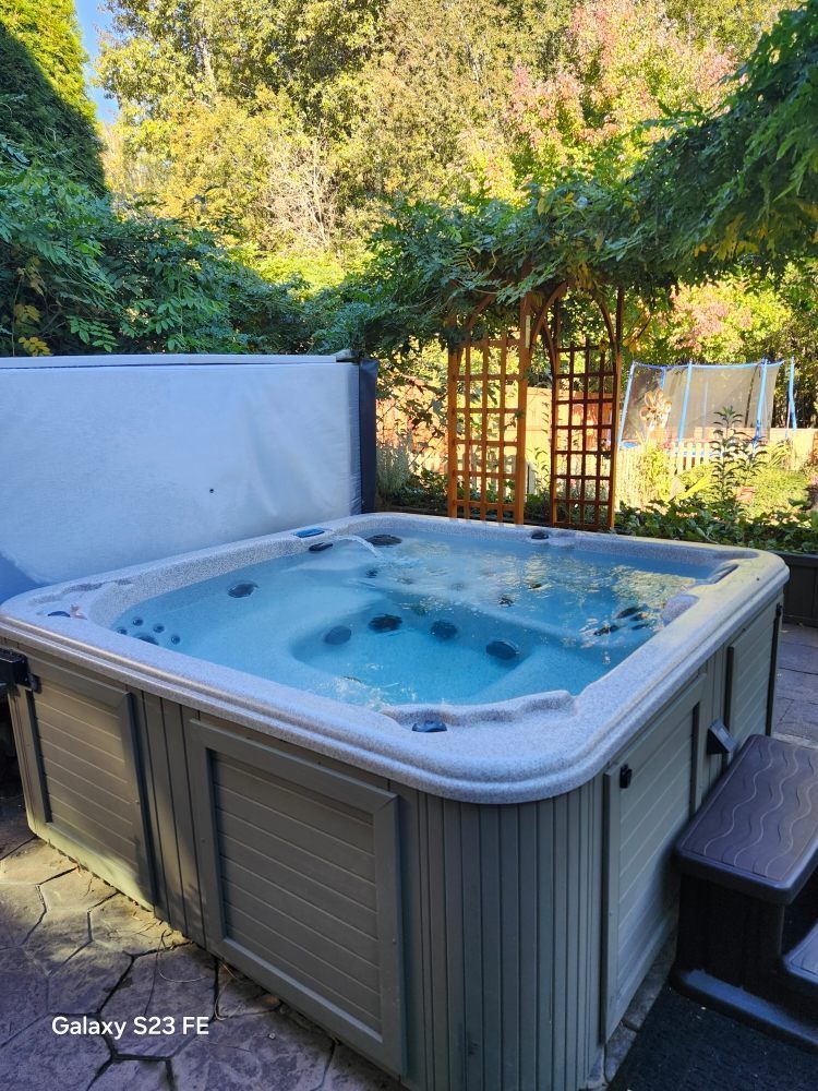 A large hot tub is sitting on a patio next to trees.