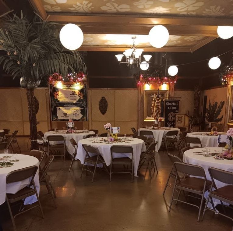 A large room filled with tables and chairs and a banner that says sponsors for the luau