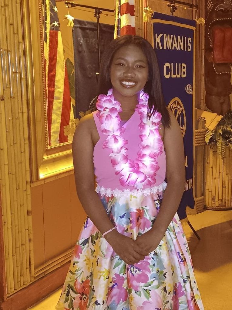 A woman in a floral dress is standing in front of a k. manis club banner