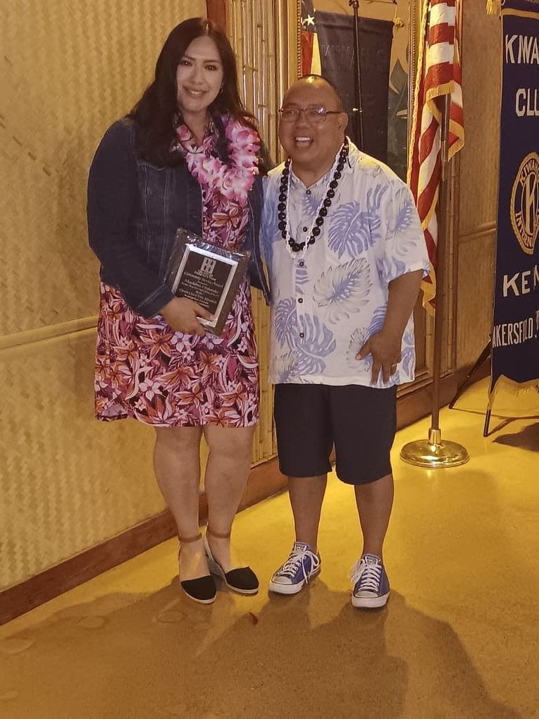A man and a woman are posing for a picture in front of a flag that says ken