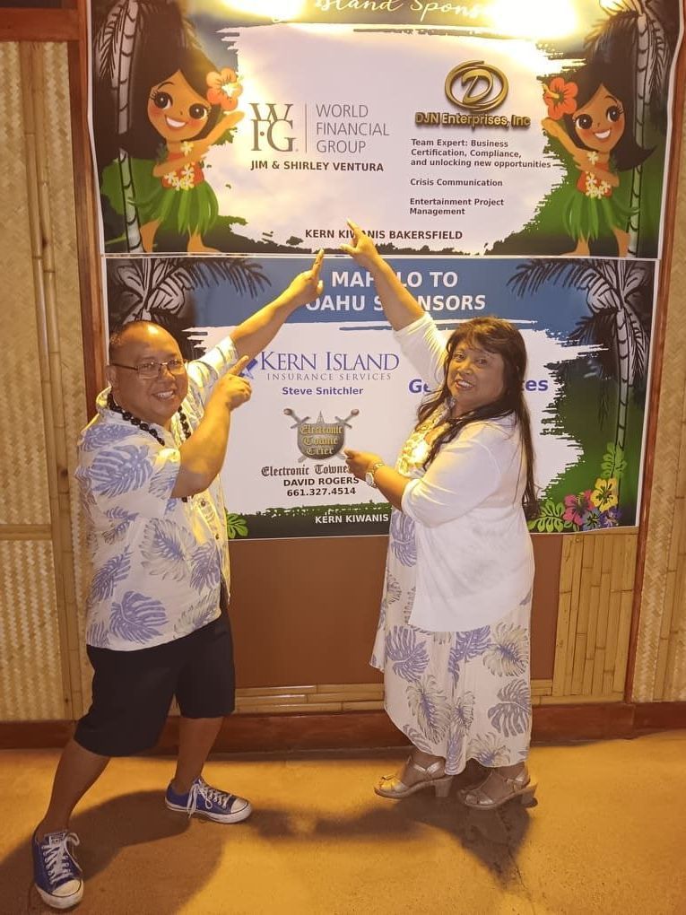A man and a woman are posing for a picture in front of a hawaiian poster.