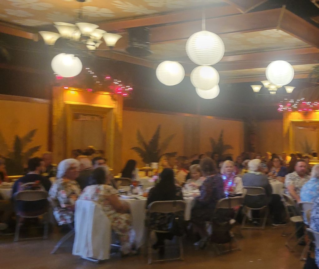 A group of people are sitting at tables in a large room with lanterns hanging from the ceiling.