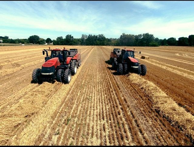 Red tractor in a field, under a blue sky, performing agricultural work.