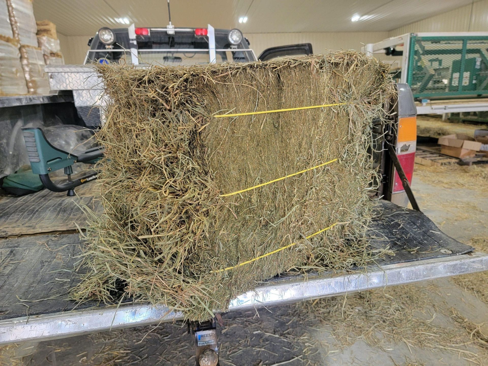 Square hay bale secured with yellow twine on a truck bed, with a vehicle in the background.