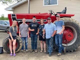 Family standing in front of a large red tractor.