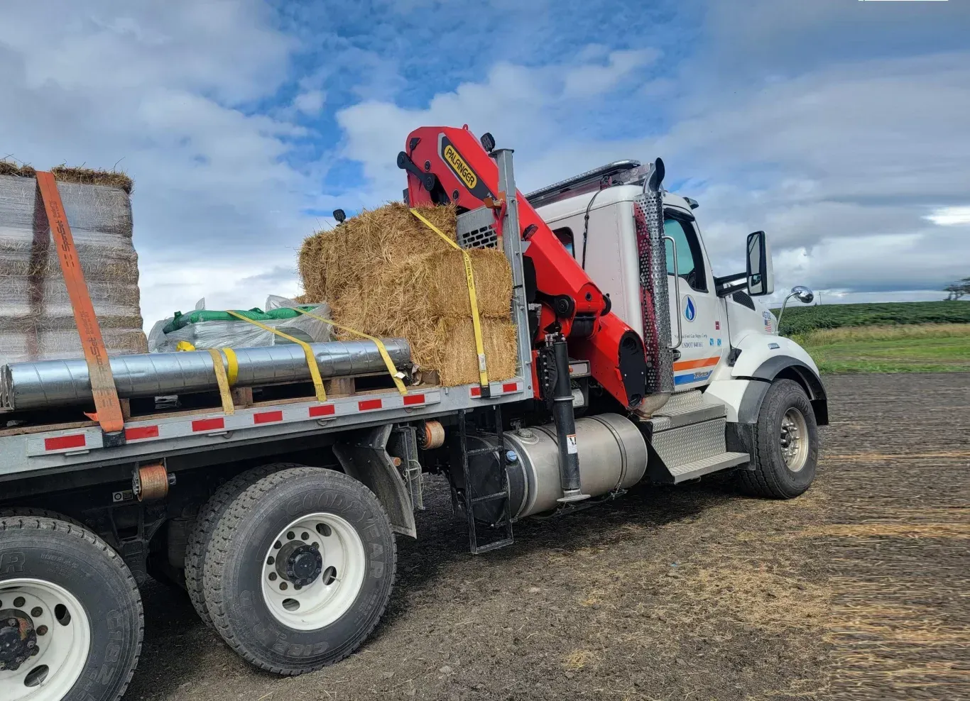 Truck bed loaded with construction materials, a hydraulic crane deployed, under a cloudy sky.