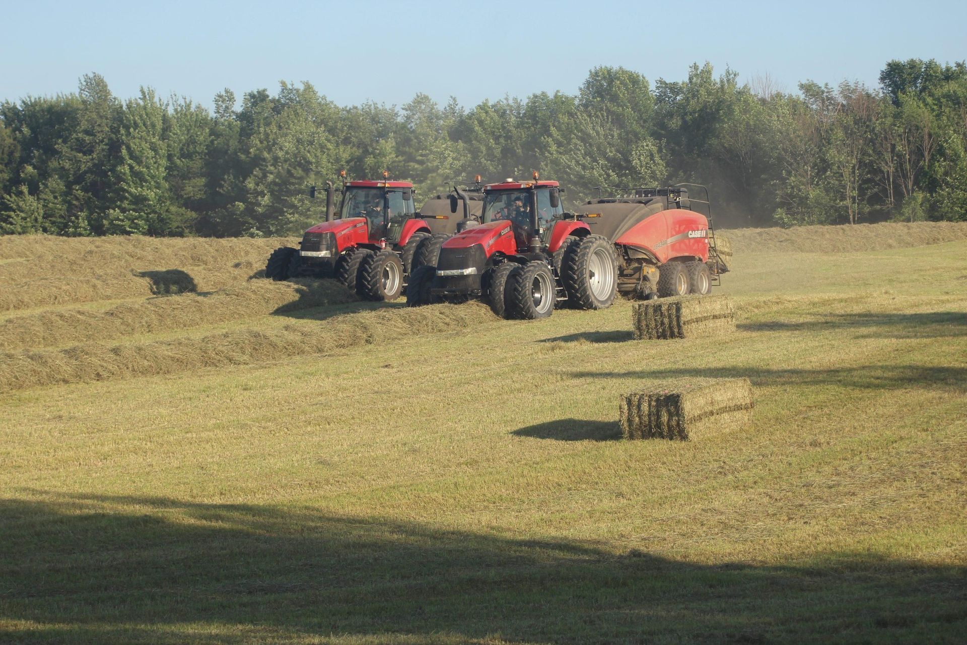 Two red tractors in a field baling hay on a sunny day.