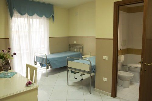una camera con due letti ospedalieri, una scrivania e vista di un bagno
