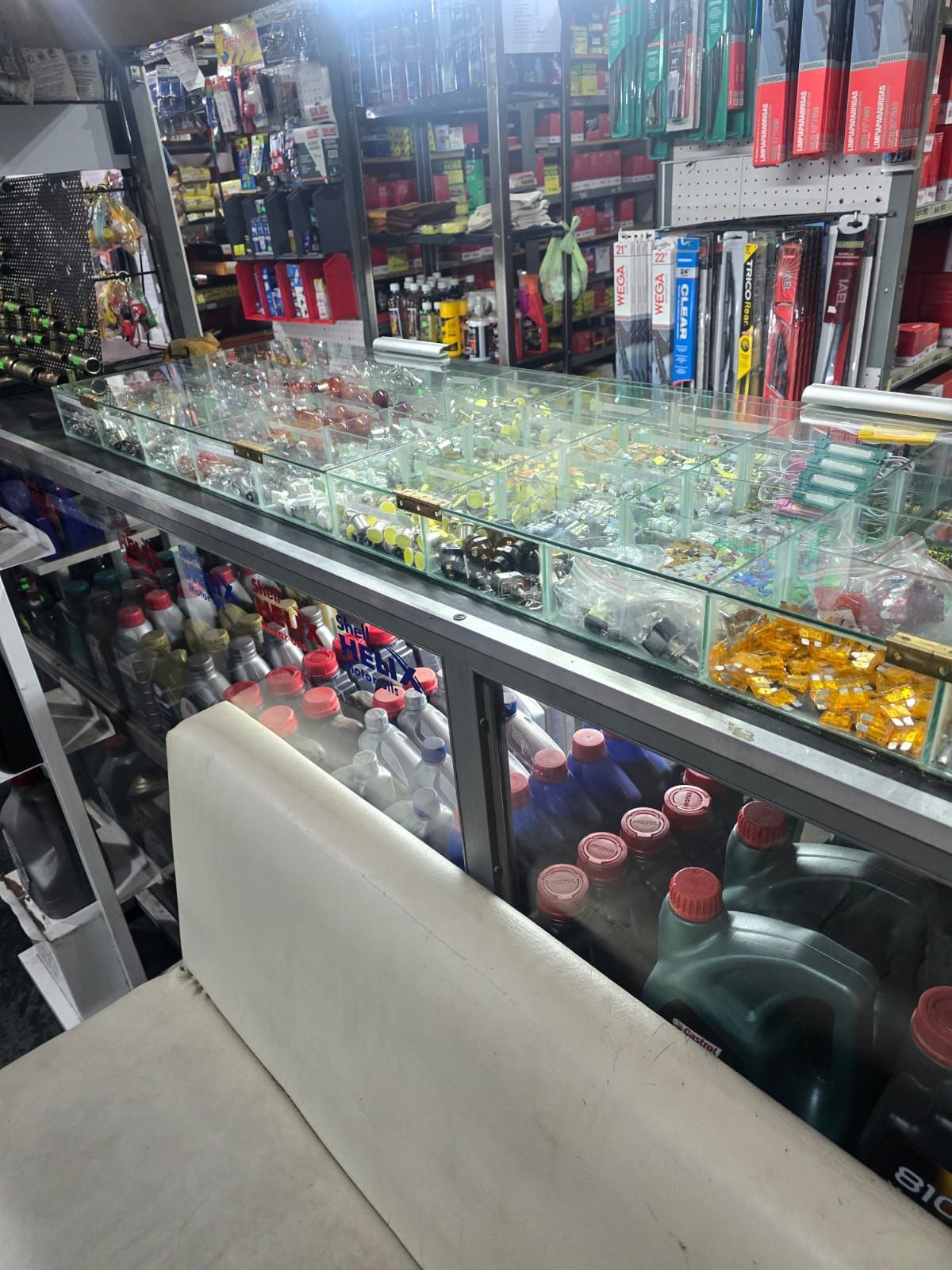 Interior de tienda de repuestos de automóviles con vitrinas de vidrio, botellas y mercancías variadas.