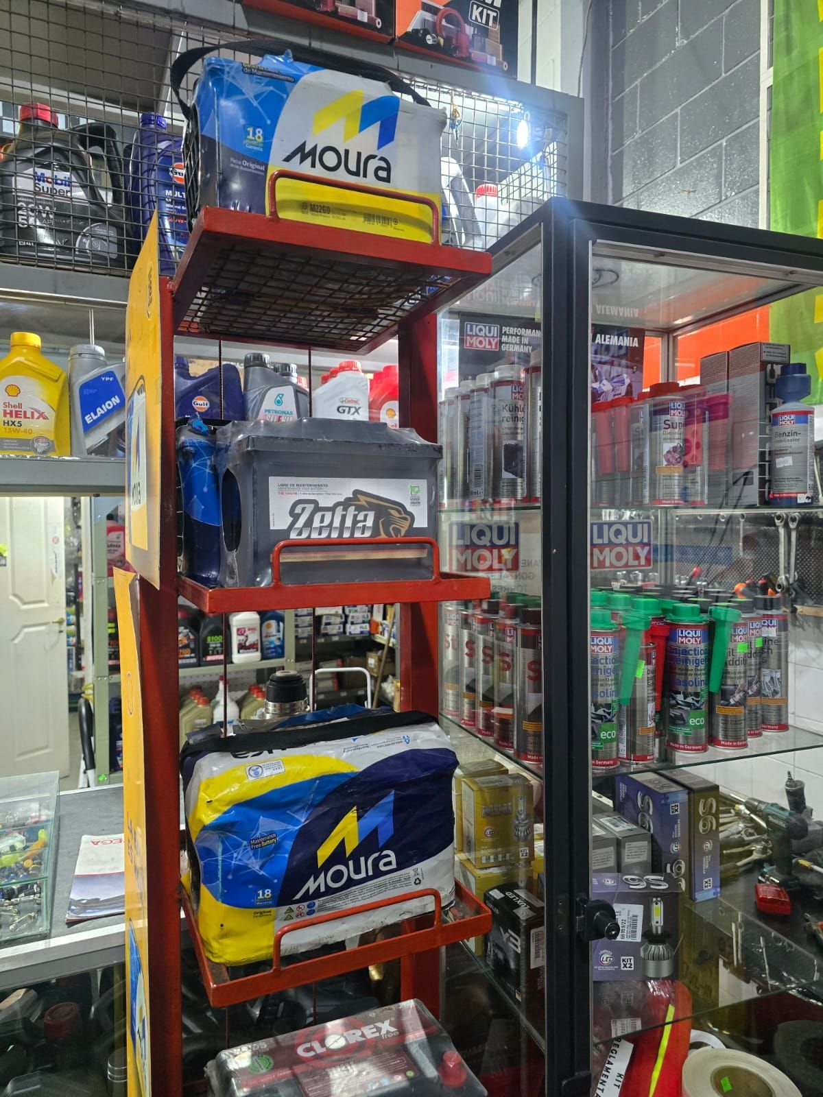 Estantes que muestran baterías de automóviles en un entorno de tienda; las marcas incluyen Moura y Zetta.