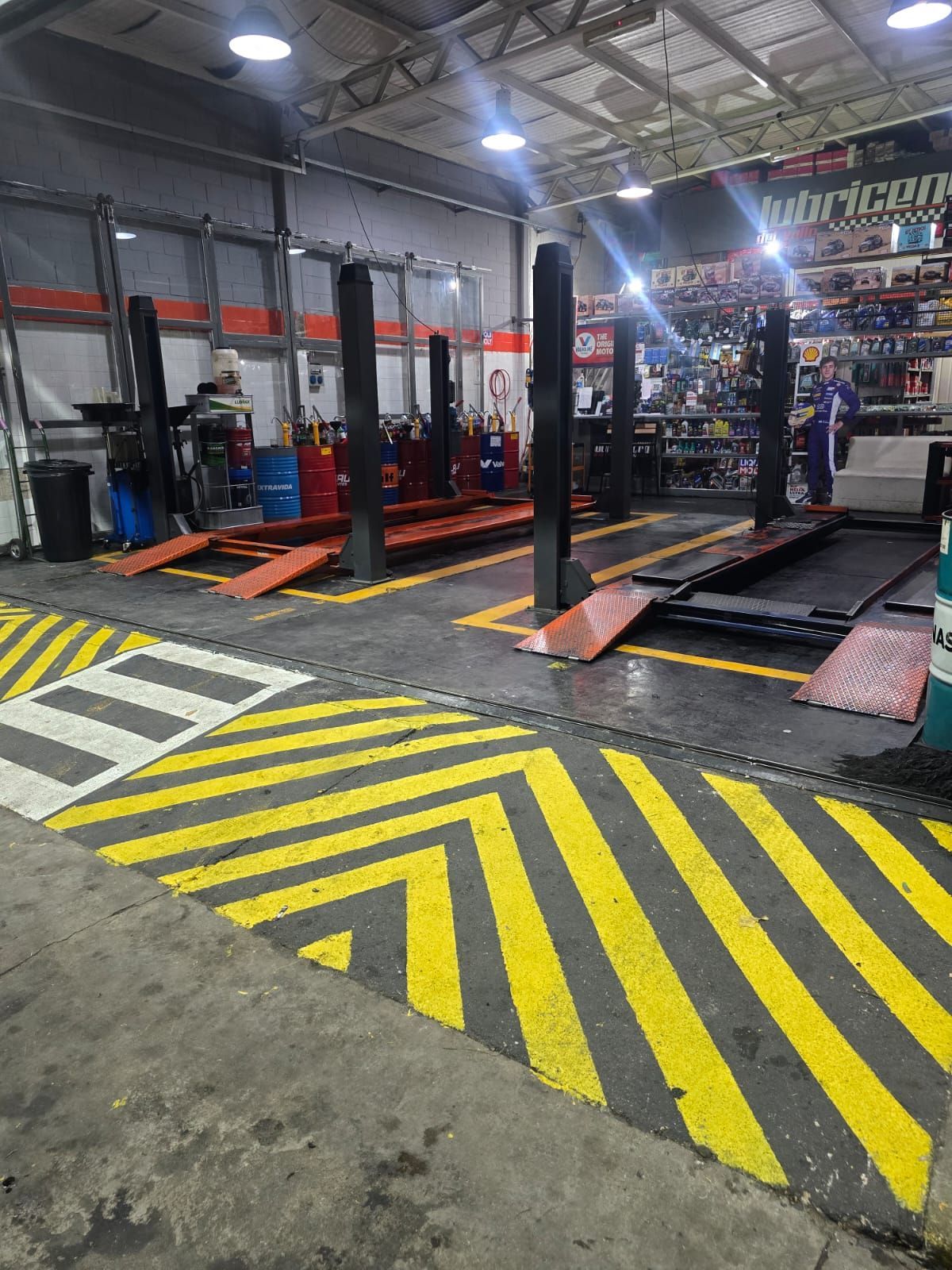 Taller de reparación de automóviles con elevadores para vehículos y marcas en el suelo con rayas amarillas y negras.