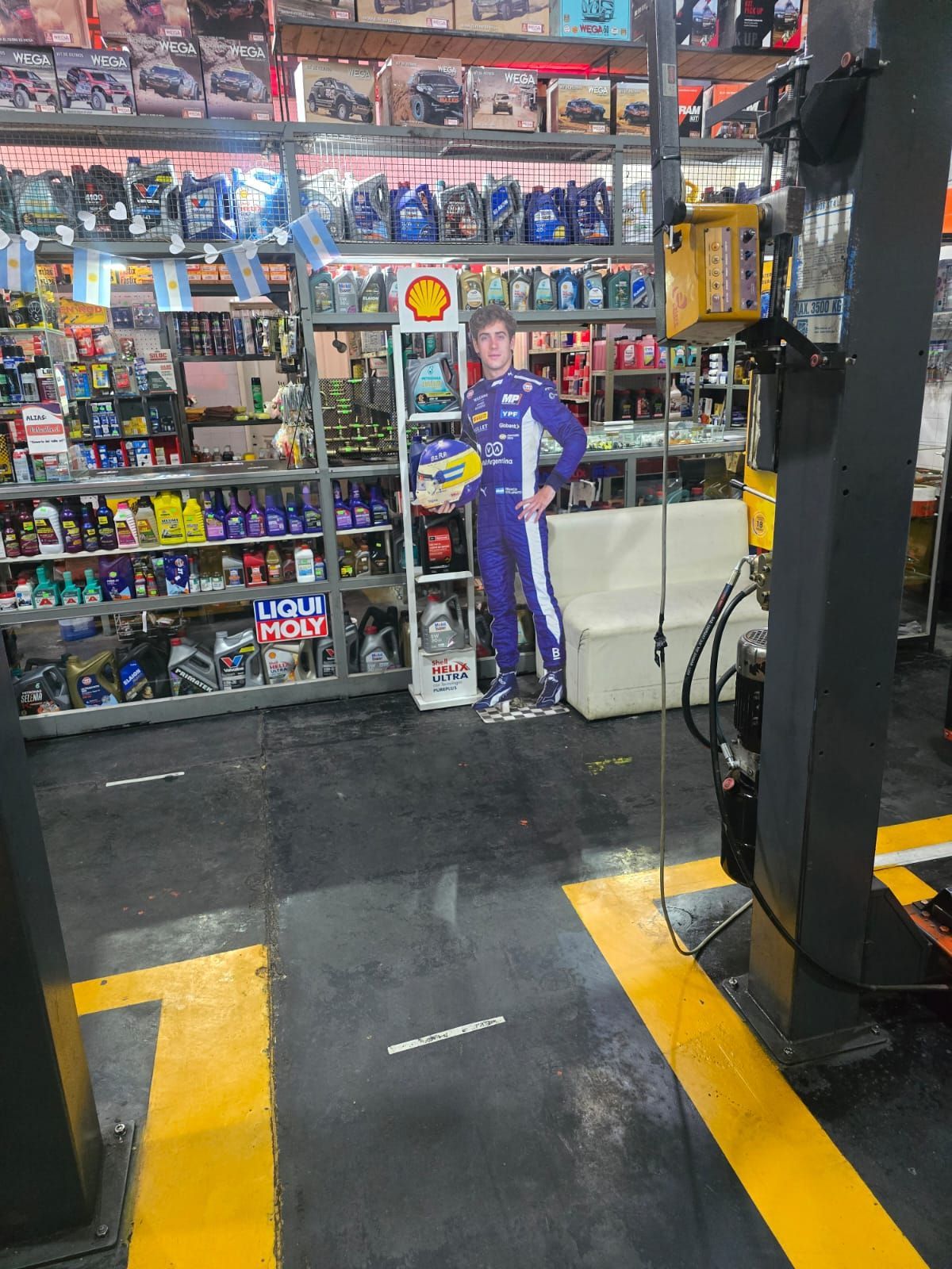 Dentro de una tienda de repuestos para automóviles; recorte de un piloto de carreras cerca de estantes de líquidos.