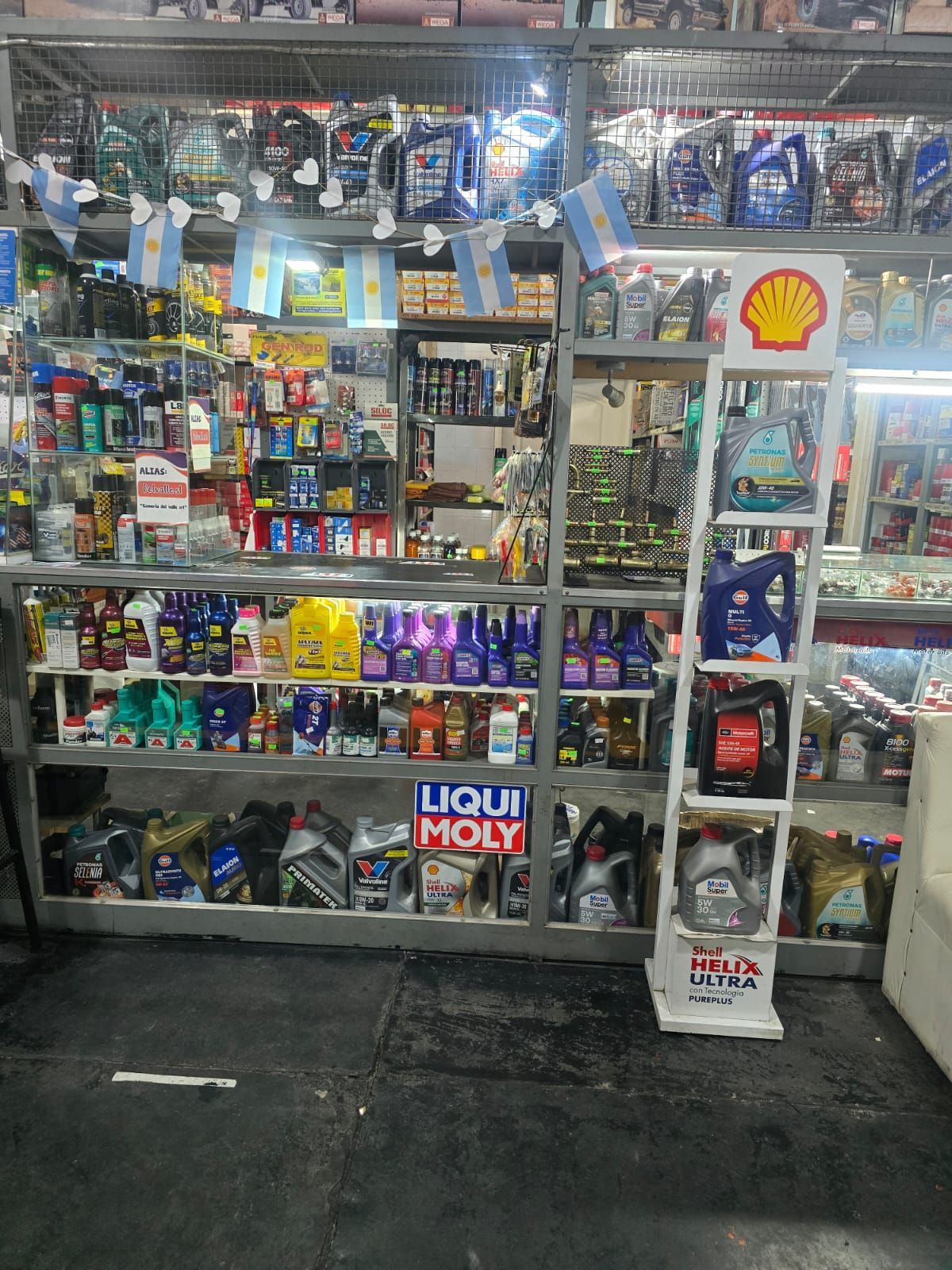 Un expositor de tienda con estanterías con diversos líquidos y productos para el automóvil, con un anuncio de Shell.