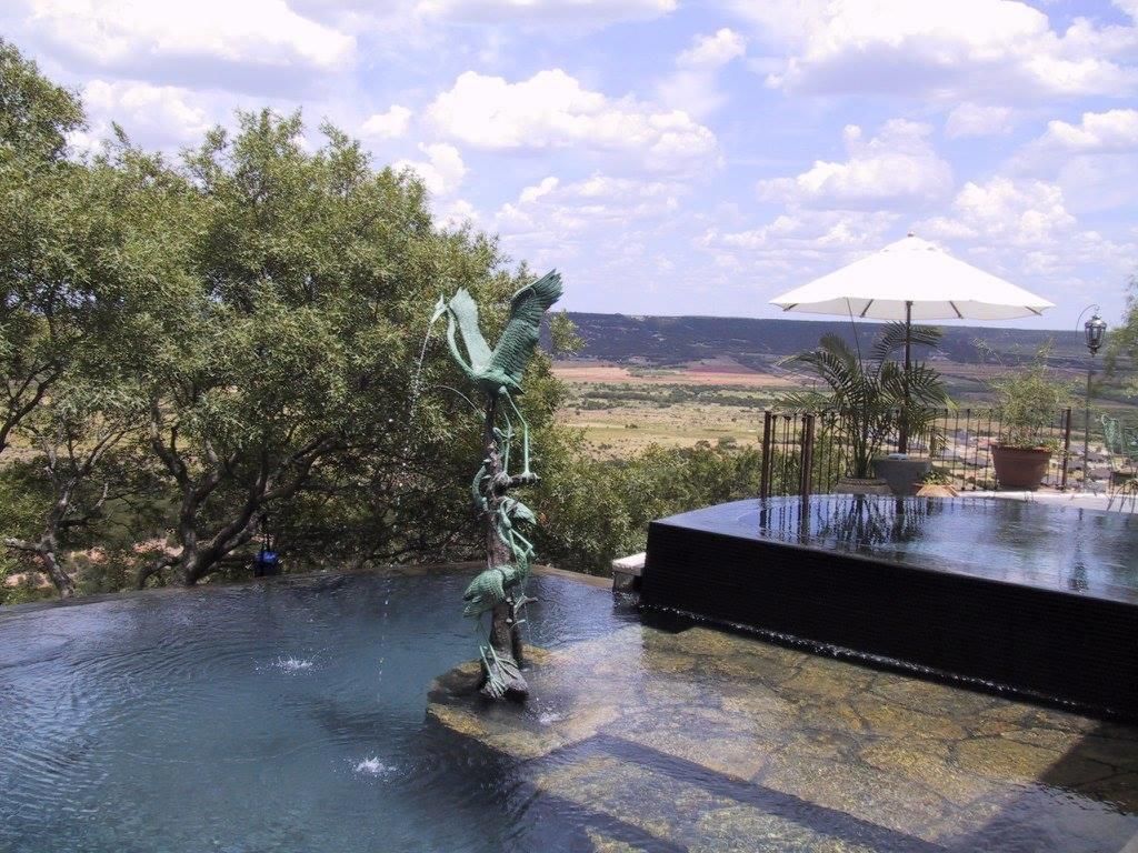 Infinity pool with fountain sculpture overlooking a vast landscape under a cloudy sky.