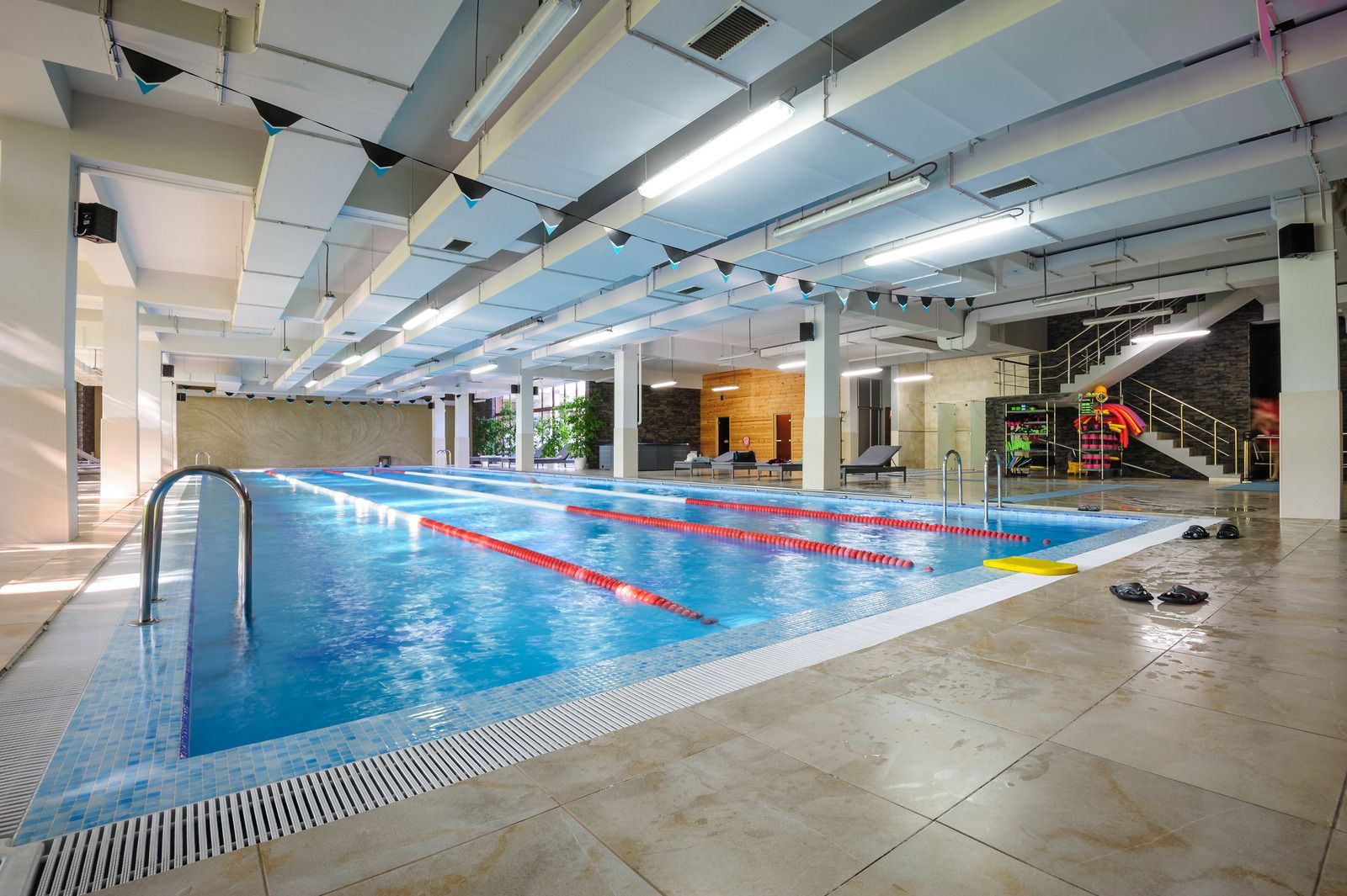Indoor swimming pool with blue water and lane markers; bright lighting.
