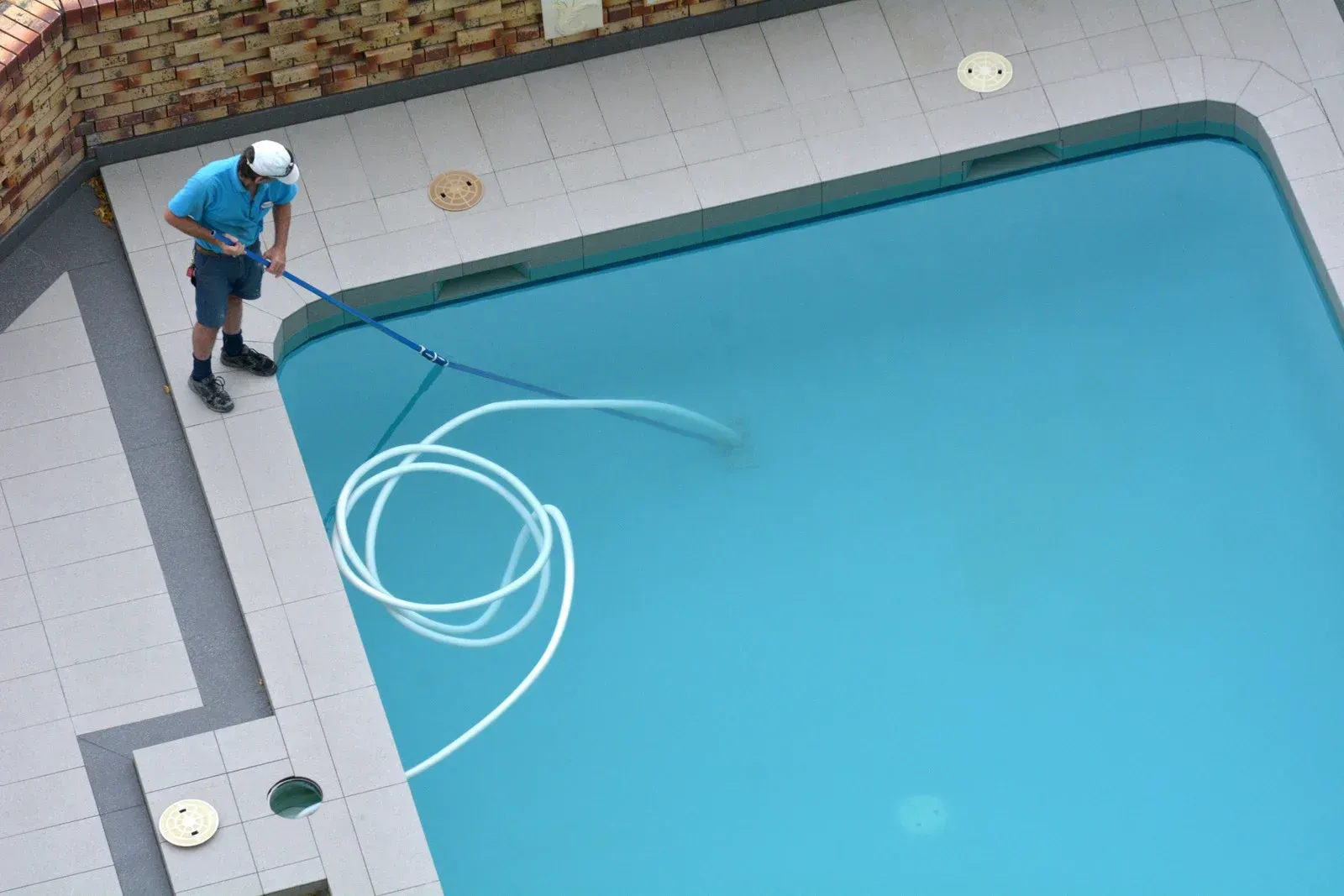 A person cleaning a rectangular swimming pool with a net and hose.