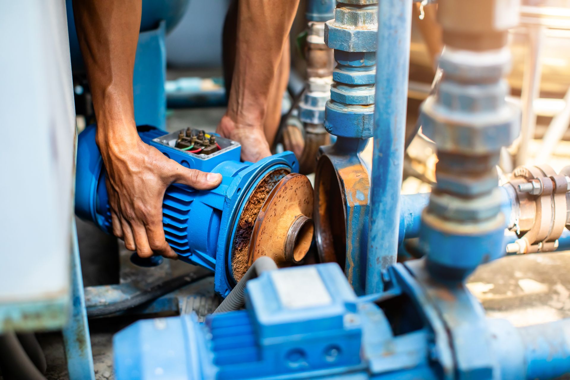 Hands of a plumber repairing and removing the motor of a centrifugal water pump.