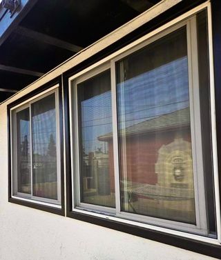 Two side-by-side sliding glass windows with gray metal frames and dark brown trim mounted on a light-colored wall.