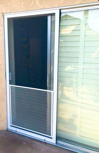 A white sliding screen door with a decorative metal pet guard at the bottom, installed on a patio door.