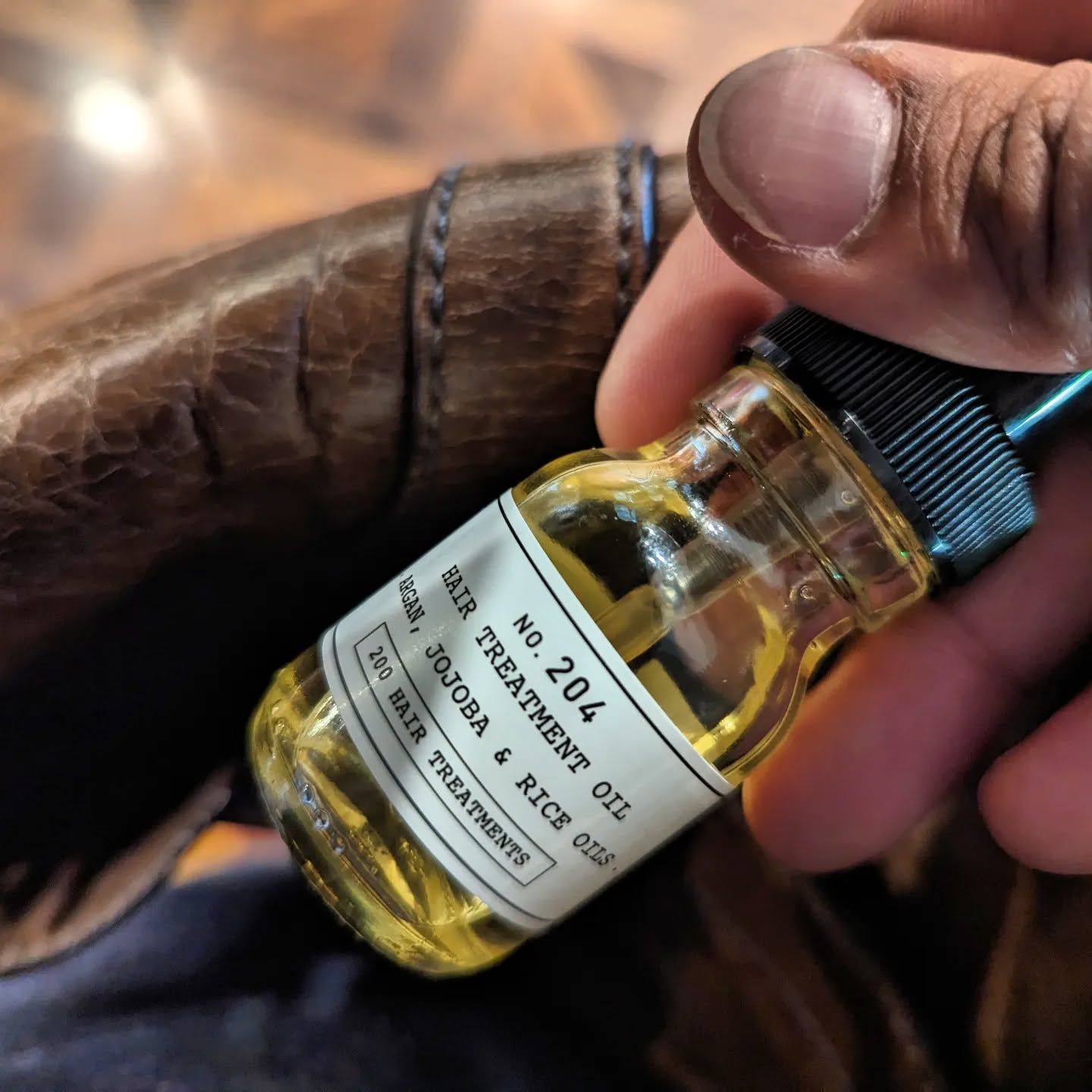 A Person is Holding a Bottle of No 204 Hair Treatment Oil — Connolly & Co Barbers In Robina, QLD