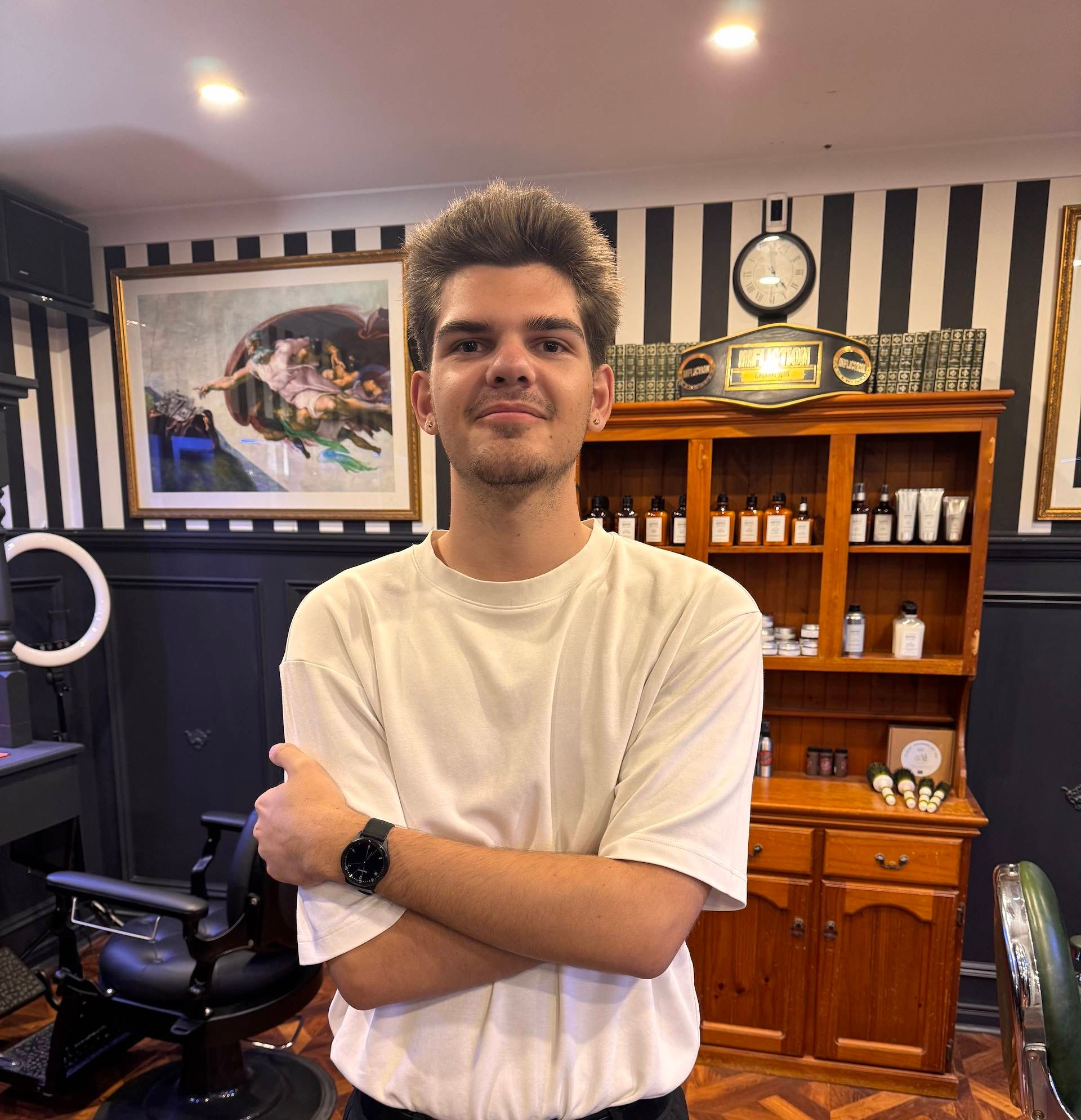 Person standing with arms crossed in a barber shop, with black-and-white striped walls and wooden decor. — Connolly & Co Barbers In Robina, QLD