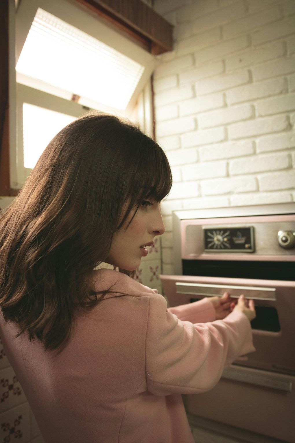 Woman in pink jacket opening pink oven in kitchen.