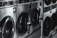 Row of industrial washing machines in a laundromat, black and white.
