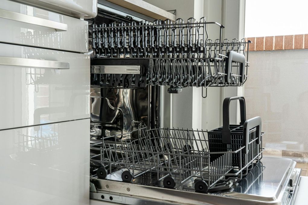 Open dishwasher with empty racks, indoors.