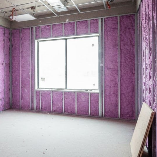Interior room under construction with pink insulation in the walls, window, bare floor.