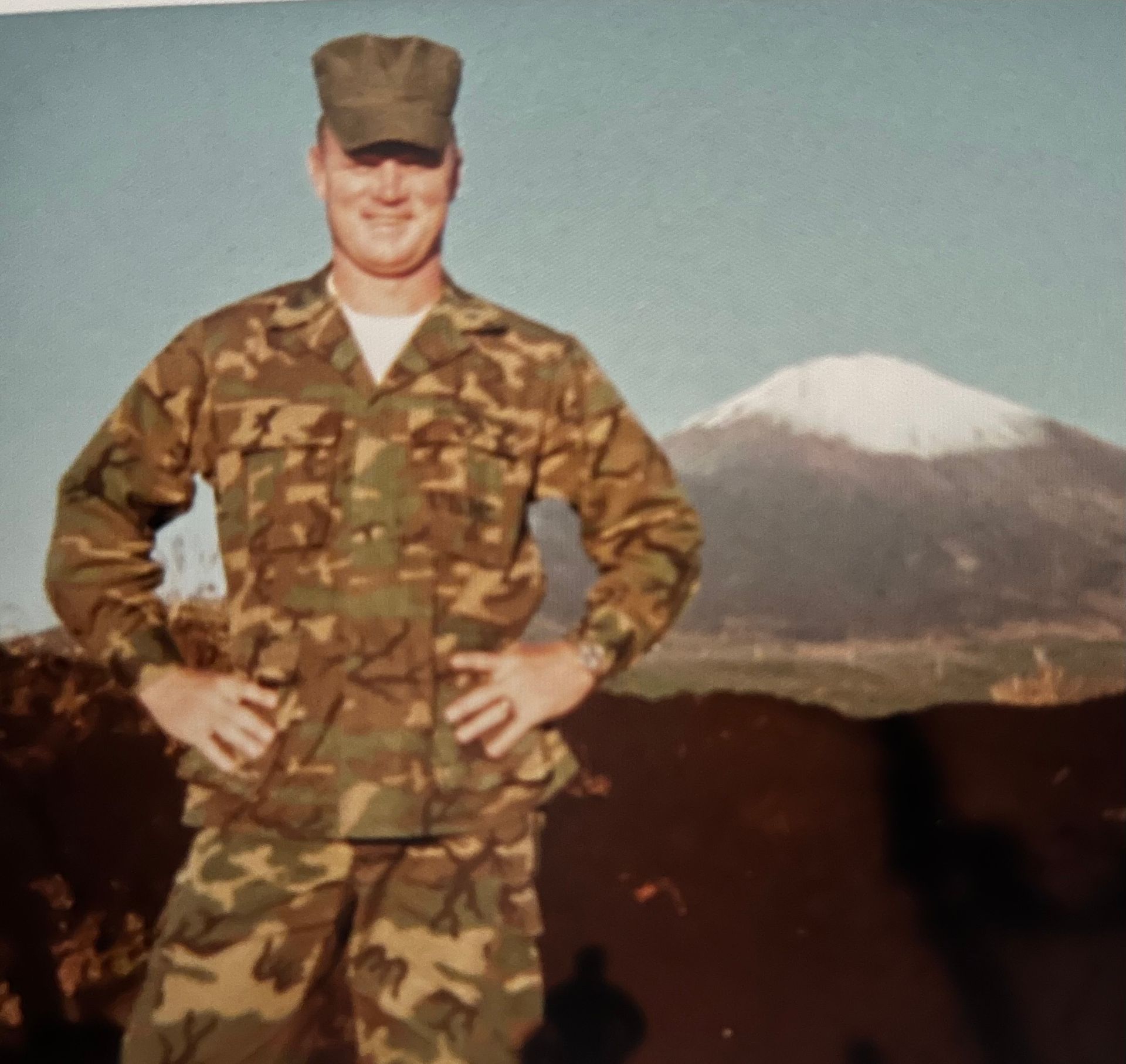 A man in a military uniform stands in front of a mountain