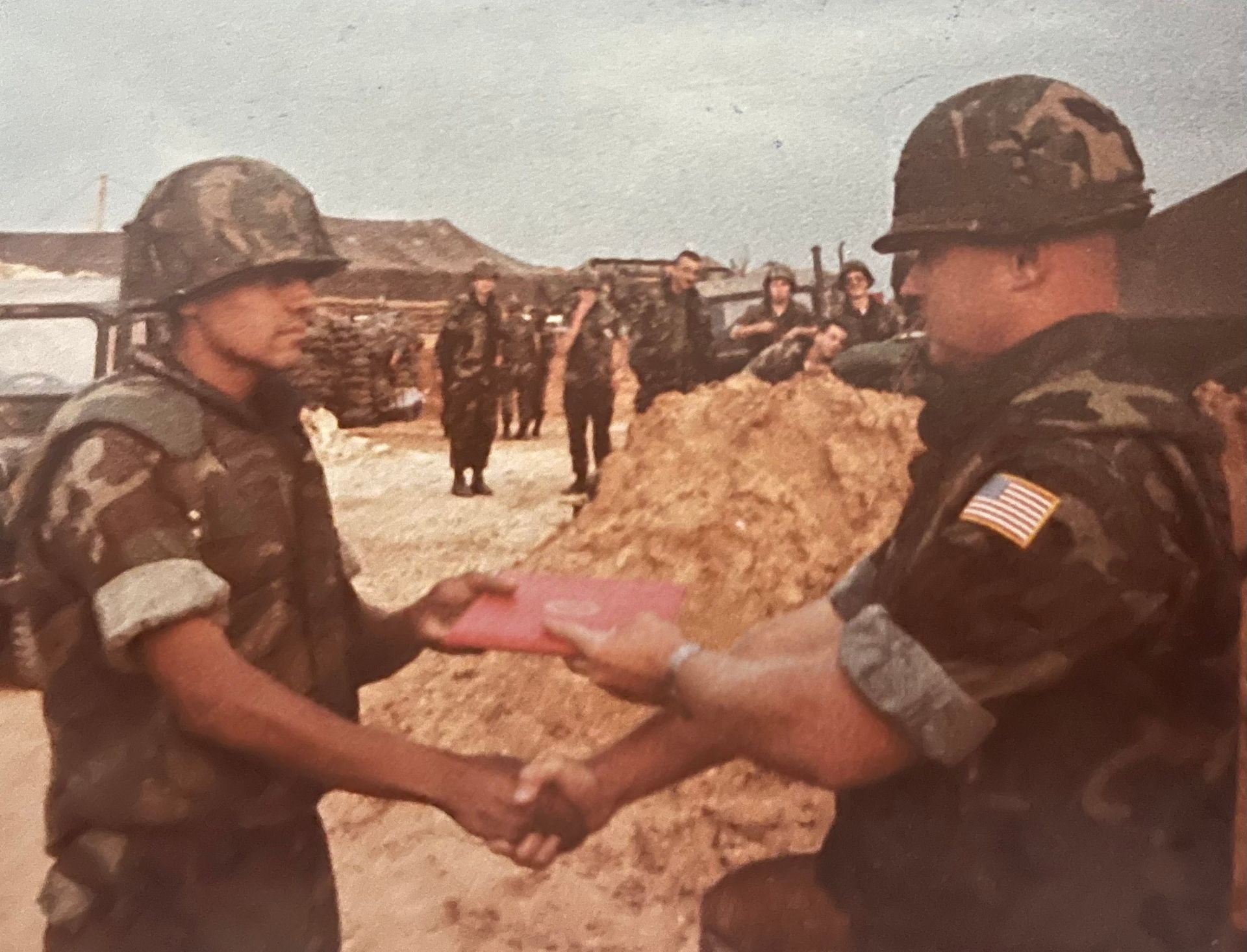 Two soldiers shaking hands in front of a pile of sand