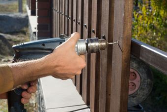 Man hands drilling wooden fence to metal construction. Building a wooden fence with a drill and screw. Close up of his hand and the tool in a DIY concept.