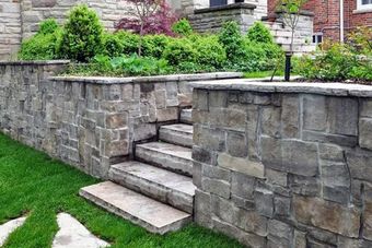 A seat wall with pillars and natural stone coping helps define a tumbled paver driveway and is a beautiful landscaping feature.