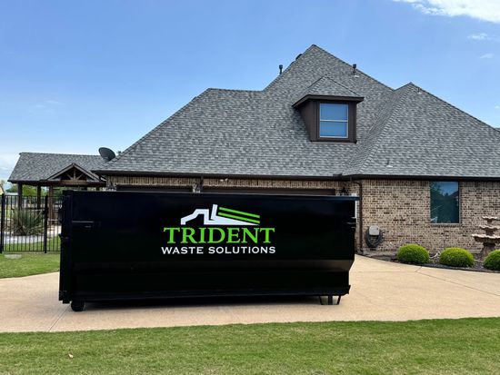 A green dumpster is parked in front of a house.