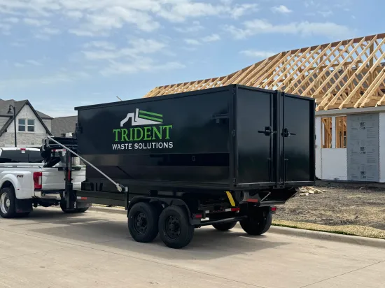 A green dumpster filled with wood is parked in front of a house.