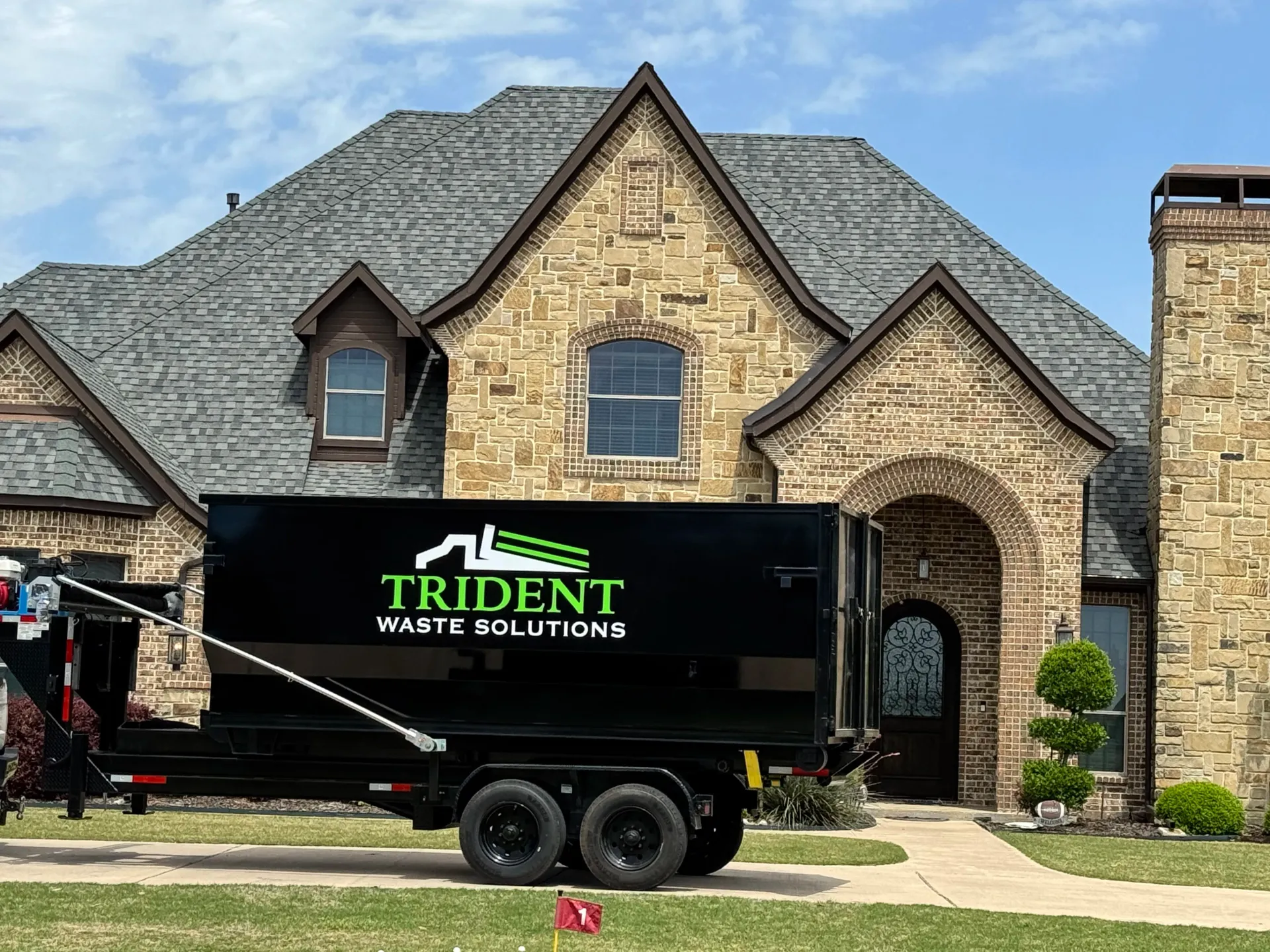 A green dumpster truck is parked on the side of the road.
