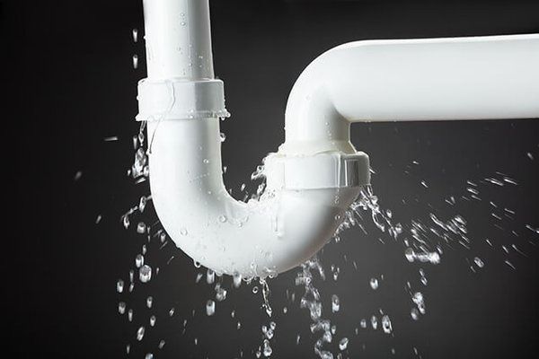 White PVC pipe leaking water against a dark background.