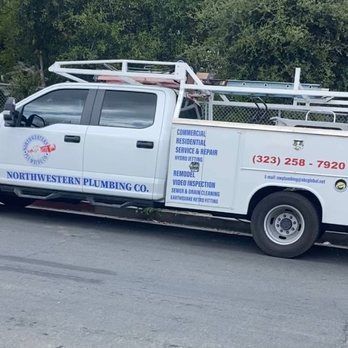White Northwestern Plumbing Co. truck parked on a street; has a rack with ladders; phone number and services listed on side.