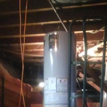 A water heater in an attic, with wooden beams and a metal ladder visible.