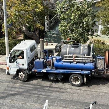 A white truck with a blue sewer cleaning apparatus parked on a street.
