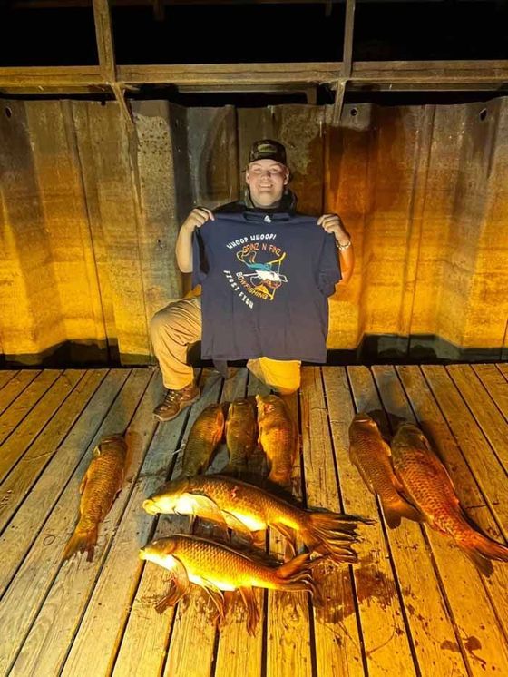 A man is holding a t-shirt in front of a pile of fish on a dock.