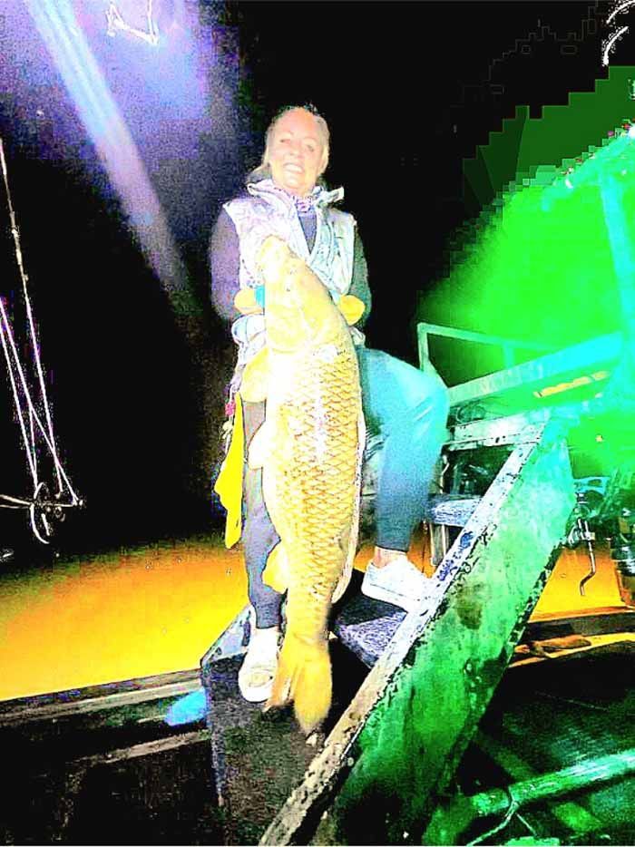 A woman is sitting on a boat holding a large fish.