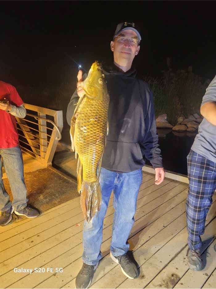 A man is holding a large fish on a dock at night.