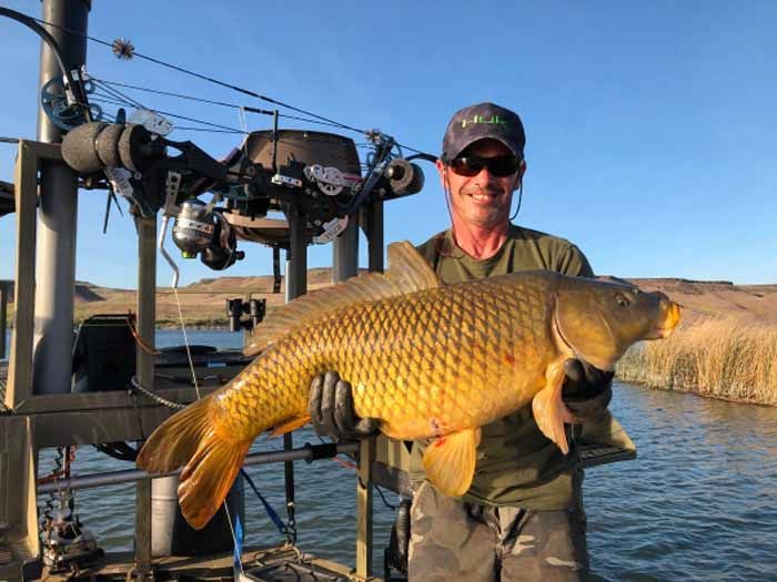 A man is holding a large carp on a boat.