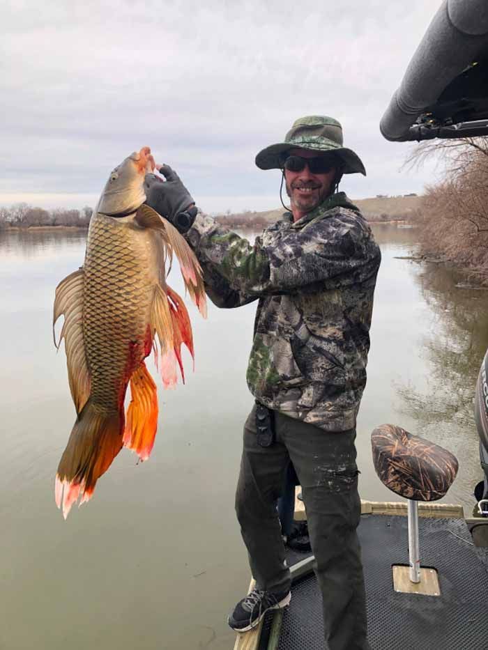 A man is standing on a boat holding a large fish.