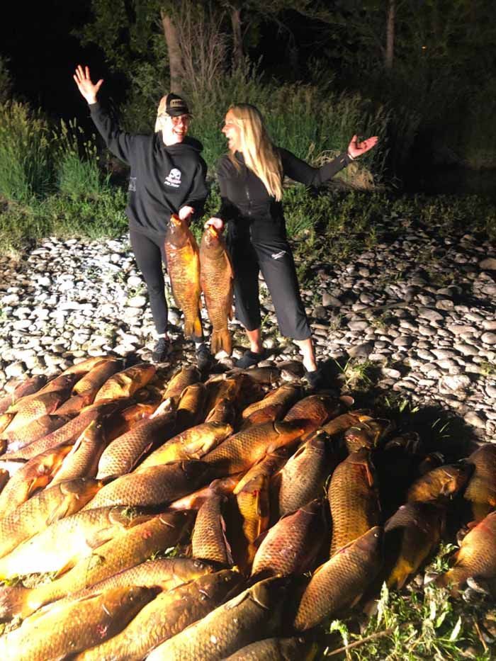 Two women are standing on top of a pile of fish.